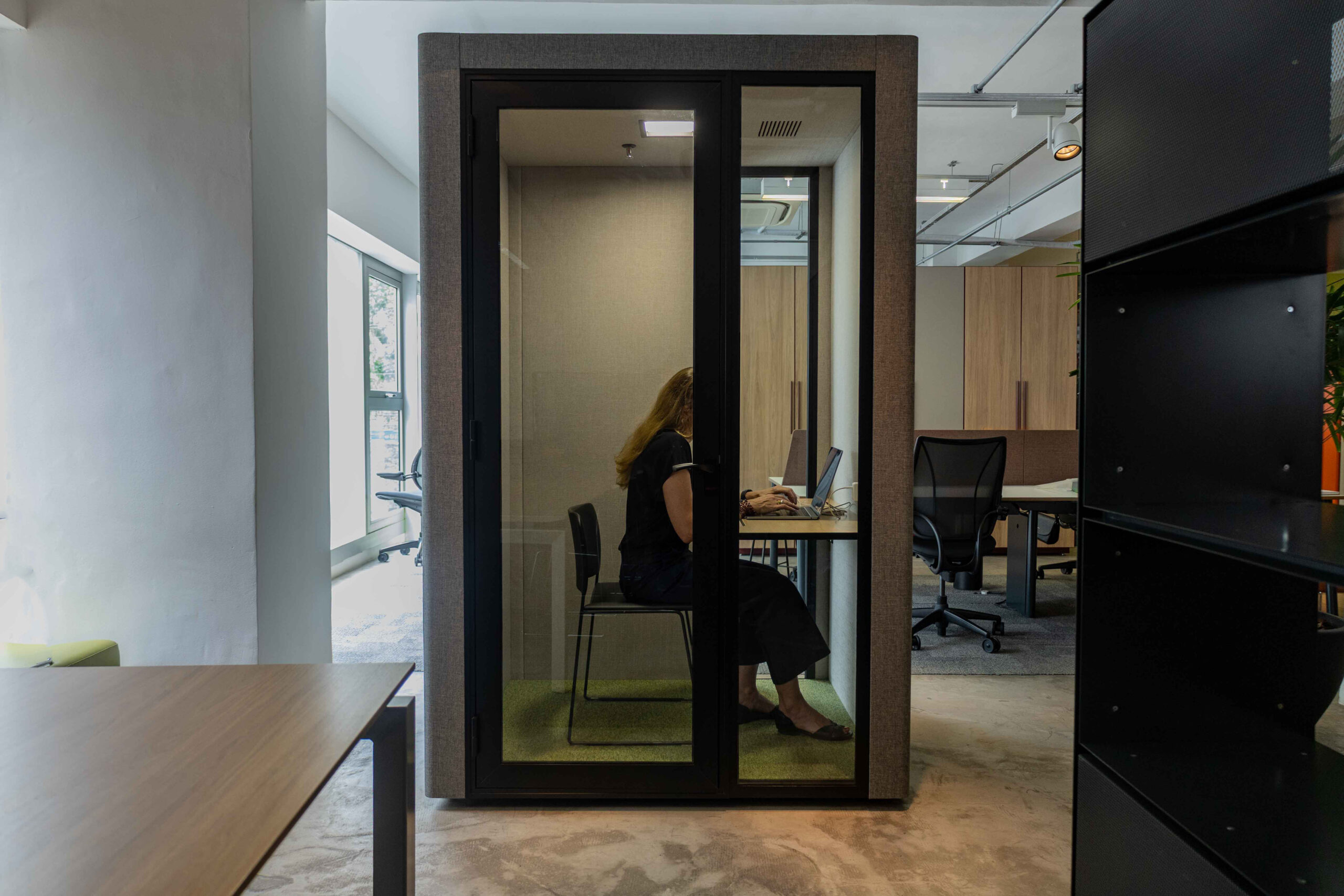 Cabine acústica individual Securit, com uma mulher loira dentro, sentada em uma cadeira.